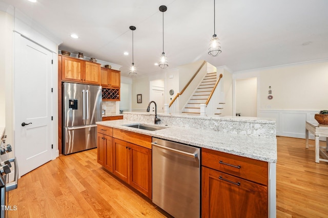 kitchen with pendant lighting, sink, a kitchen island with sink, stainless steel appliances, and light hardwood / wood-style floors