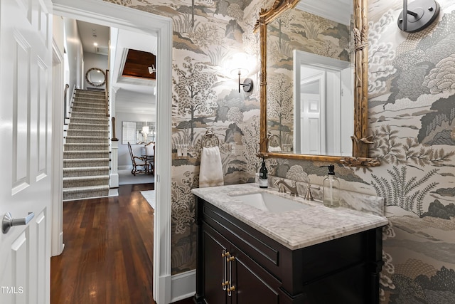 bathroom with ornamental molding, wood finished floors, vanity, and wallpapered walls