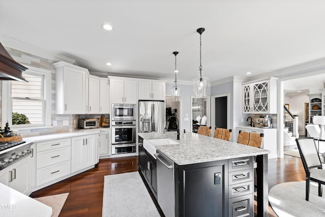 kitchen featuring white cabinets, ornamental molding, a kitchen island with sink, stainless steel appliances, and a sink