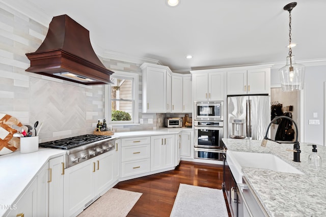 kitchen featuring crown molding, custom range hood, appliances with stainless steel finishes, dark wood-type flooring, and white cabinets