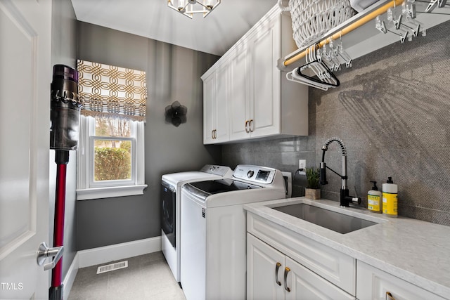 clothes washing area featuring washer and clothes dryer, cabinet space, visible vents, a sink, and baseboards