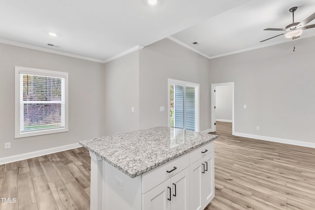 kitchen with white cabinets, ornamental molding, a center island, light stone counters, and light wood-type flooring