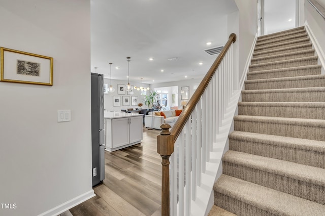 stairs with hardwood / wood-style floors and a chandelier