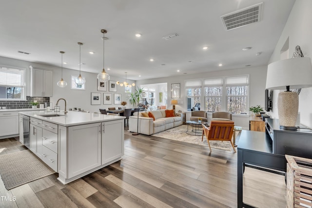 kitchen with sink, white cabinetry, backsplash, hanging light fixtures, and a center island with sink