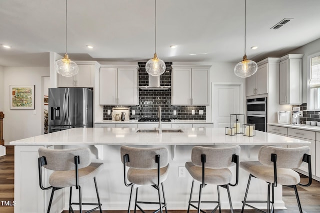 kitchen with hanging light fixtures, stainless steel appliances, an island with sink, and white cabinets