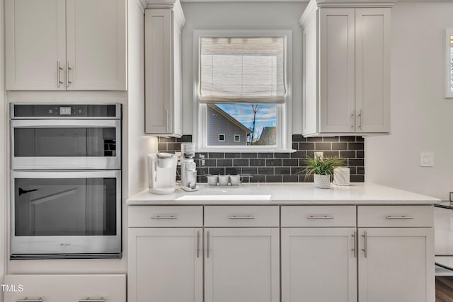 kitchen with white cabinetry, decorative backsplash, light stone countertops, and stainless steel double oven