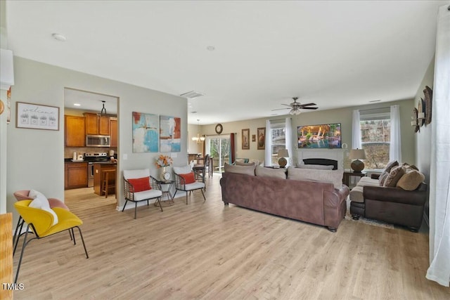 living room with ceiling fan with notable chandelier and light wood-type flooring