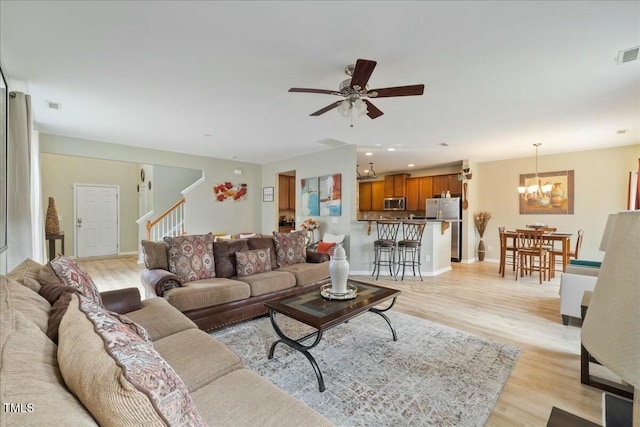 living room featuring ceiling fan with notable chandelier and light hardwood / wood-style flooring