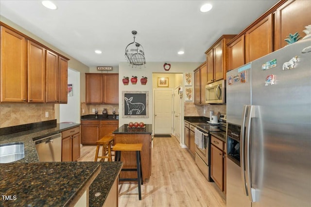 kitchen with appliances with stainless steel finishes, a kitchen breakfast bar, decorative backsplash, decorative light fixtures, and light wood-type flooring