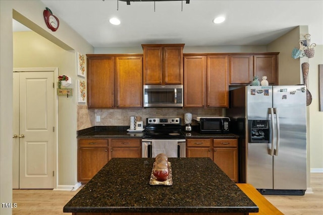 kitchen with backsplash, light hardwood / wood-style flooring, stainless steel appliances, and dark stone counters