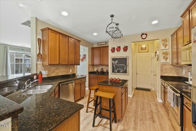 kitchen featuring pendant lighting, sink, light hardwood / wood-style flooring, a breakfast bar, and appliances with stainless steel finishes