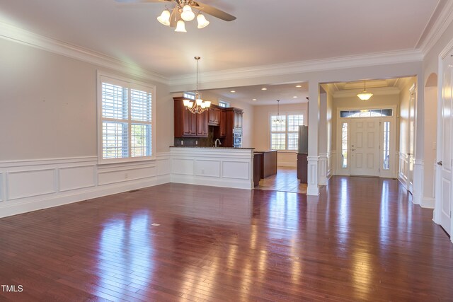 unfurnished living room with crown molding, dark wood-type flooring, and ceiling fan with notable chandelier