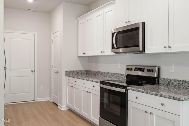 kitchen featuring white cabinetry, stainless steel appliances, light stone counters, and light wood-type flooring