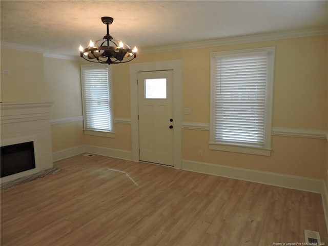 entryway featuring crown molding, a brick fireplace, hardwood / wood-style flooring, and a chandelier