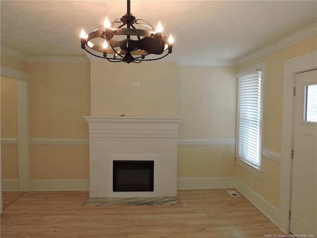 interior space with a brick fireplace, a notable chandelier, ornamental molding, and light hardwood / wood-style floors