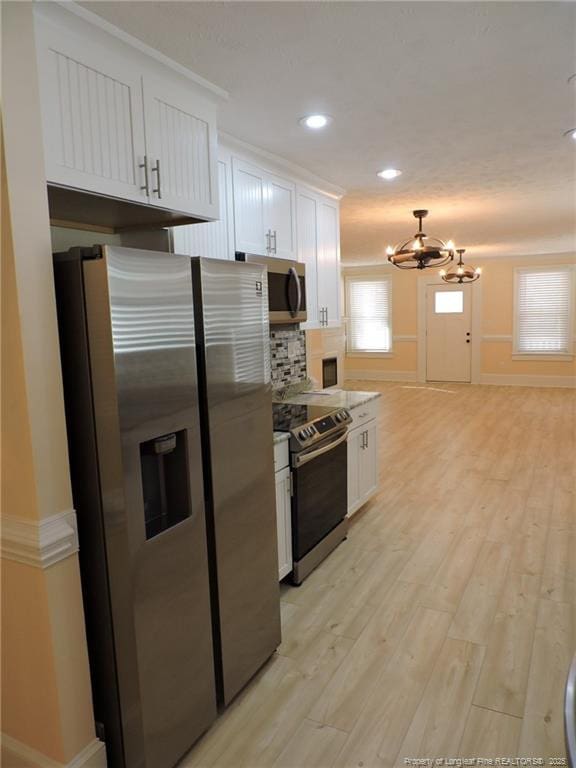 kitchen with appliances with stainless steel finishes, light hardwood / wood-style floors, hanging light fixtures, and white cabinets