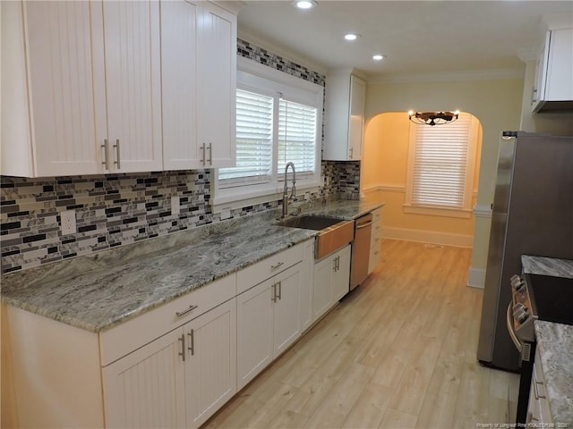 kitchen featuring appliances with stainless steel finishes, white cabinetry, sink, crown molding, and light stone countertops