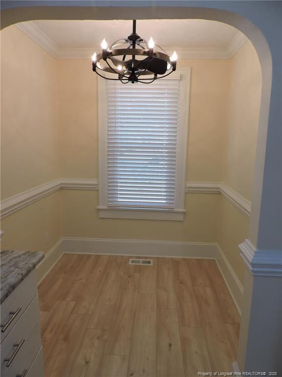 unfurnished dining area featuring an inviting chandelier, ornamental molding, and light hardwood / wood-style floors