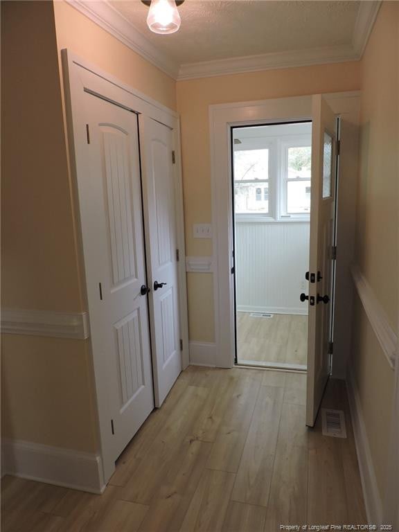 doorway with crown molding, light hardwood / wood-style floors, and a textured ceiling