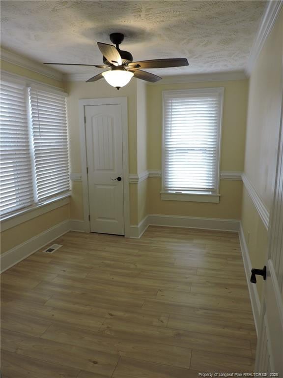 empty room featuring ceiling fan, hardwood / wood-style flooring, ornamental molding, and a textured ceiling