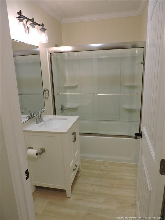 bathroom with hardwood / wood-style flooring, ornamental molding, combined bath / shower with glass door, and vanity