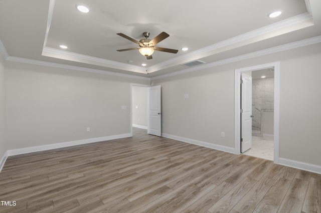 interior space with ceiling fan, connected bathroom, a tray ceiling, ornamental molding, and light hardwood / wood-style floors