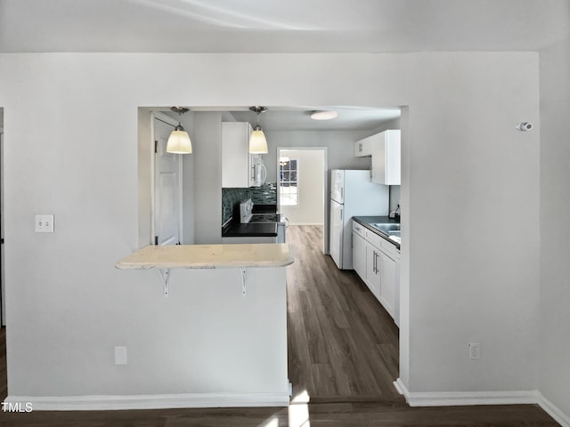 kitchen featuring pendant lighting, white appliances, a breakfast bar, white cabinetry, and kitchen peninsula