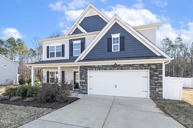 craftsman inspired home featuring a garage, stone siding, fence, and driveway