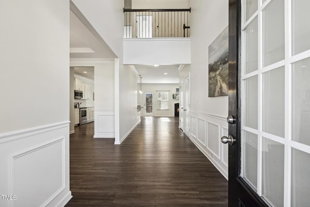 entrance foyer with a towering ceiling, a wainscoted wall, ornamental molding, dark wood-type flooring, and a decorative wall