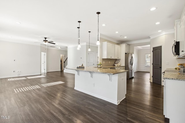 kitchen with white cabinets, appliances with stainless steel finishes, a breakfast bar, light stone counters, and decorative light fixtures