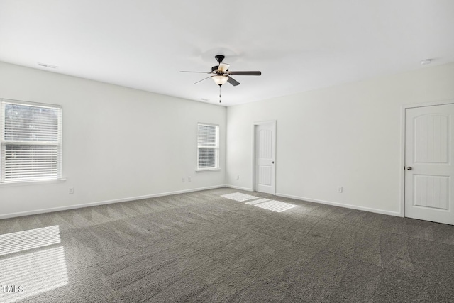 unfurnished room featuring dark carpet, plenty of natural light, a ceiling fan, and baseboards