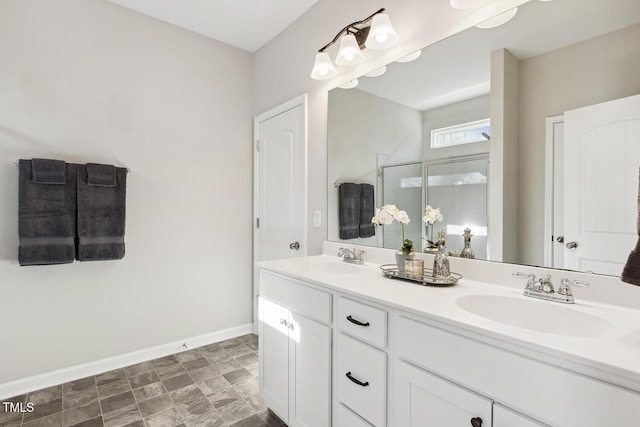 full bathroom featuring double vanity, a stall shower, baseboards, and a sink