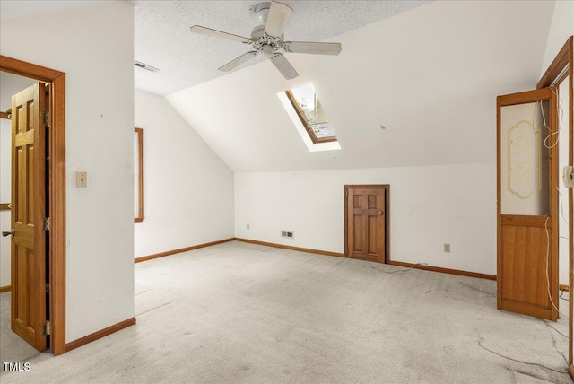 additional living space featuring ceiling fan, a textured ceiling, light colored carpet, and vaulted ceiling with skylight