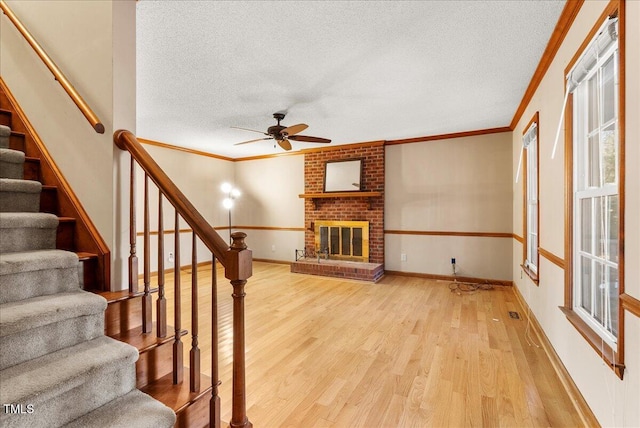 unfurnished living room with crown molding, light hardwood / wood-style flooring, plenty of natural light, a textured ceiling, and a brick fireplace