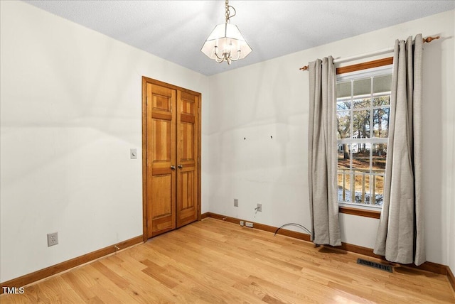 empty room featuring a textured ceiling, light hardwood / wood-style flooring, and a notable chandelier