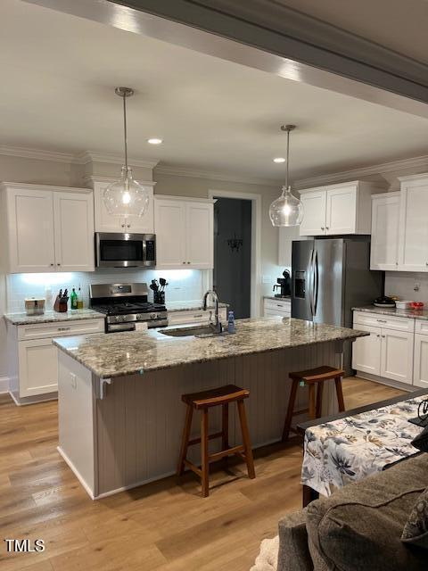 kitchen featuring sink, decorative light fixtures, appliances with stainless steel finishes, an island with sink, and light stone countertops