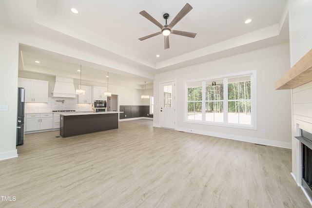 unfurnished living room with a raised ceiling, ceiling fan, and light wood-type flooring