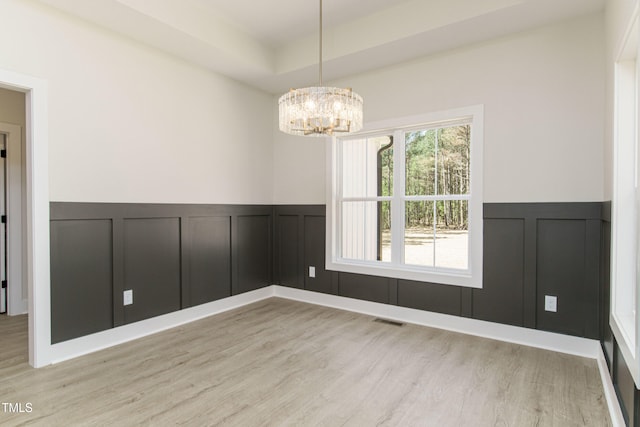 empty room with a tray ceiling, a chandelier, and light hardwood / wood-style floors