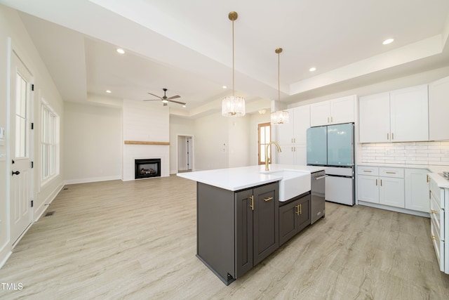 kitchen featuring white cabinetry, sink, a raised ceiling, and a center island with sink