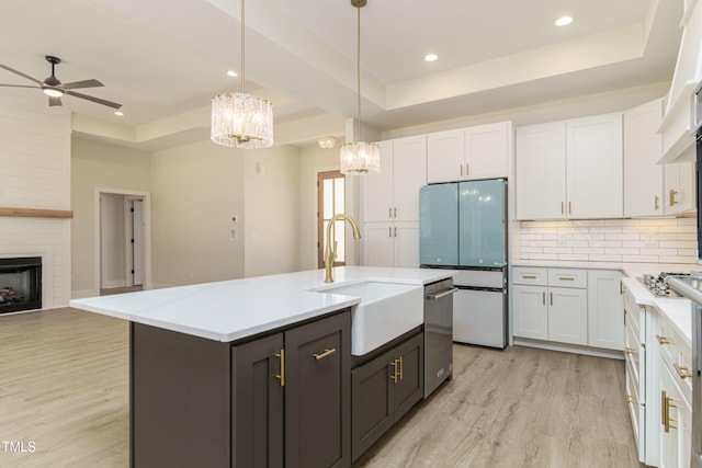 kitchen featuring a raised ceiling, sink, an island with sink, and white cabinets