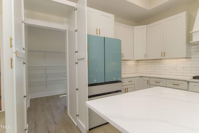 kitchen with white cabinetry, light stone counters, tasteful backsplash, and light wood-type flooring