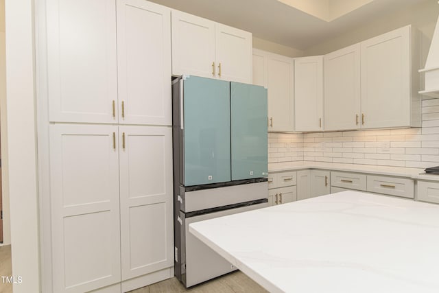 kitchen with tasteful backsplash, fridge, light stone countertops, and white cabinets