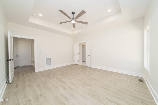 spare room featuring ceiling fan, a tray ceiling, and light hardwood / wood-style flooring