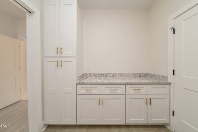 kitchen with light stone countertops, light wood-type flooring, and white cabinets