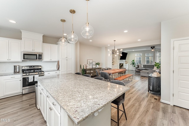 kitchen with decorative light fixtures, a kitchen island, white cabinets, and appliances with stainless steel finishes