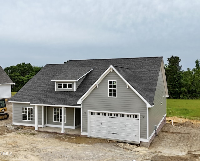 traditional-style house featuring a shingled roof, covered porch, an attached garage, and dirt driveway