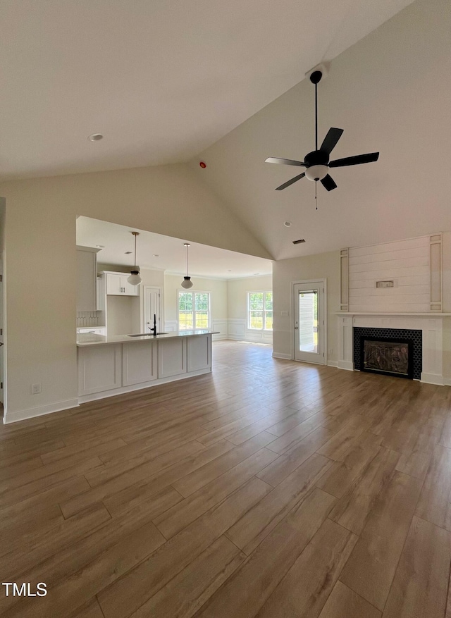 unfurnished living room with ceiling fan, wood finished floors, high vaulted ceiling, and a tile fireplace