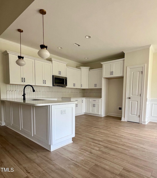 kitchen with stainless steel microwave, crown molding, white cabinetry, a peninsula, and tasteful backsplash