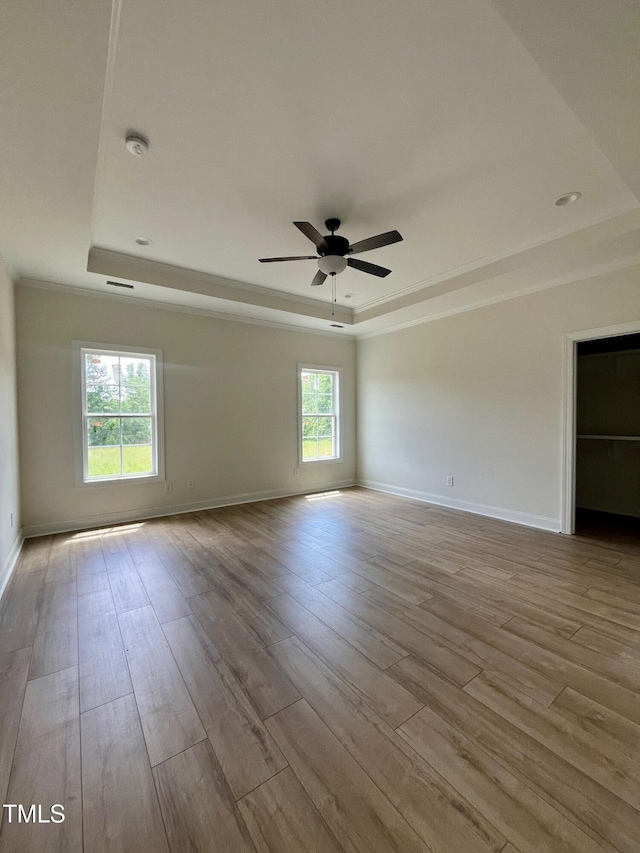 spare room featuring a tray ceiling, wood finished floors, ceiling fan, crown molding, and baseboards