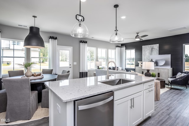 kitchen featuring sink, white cabinetry, decorative light fixtures, stainless steel dishwasher, and a kitchen island with sink